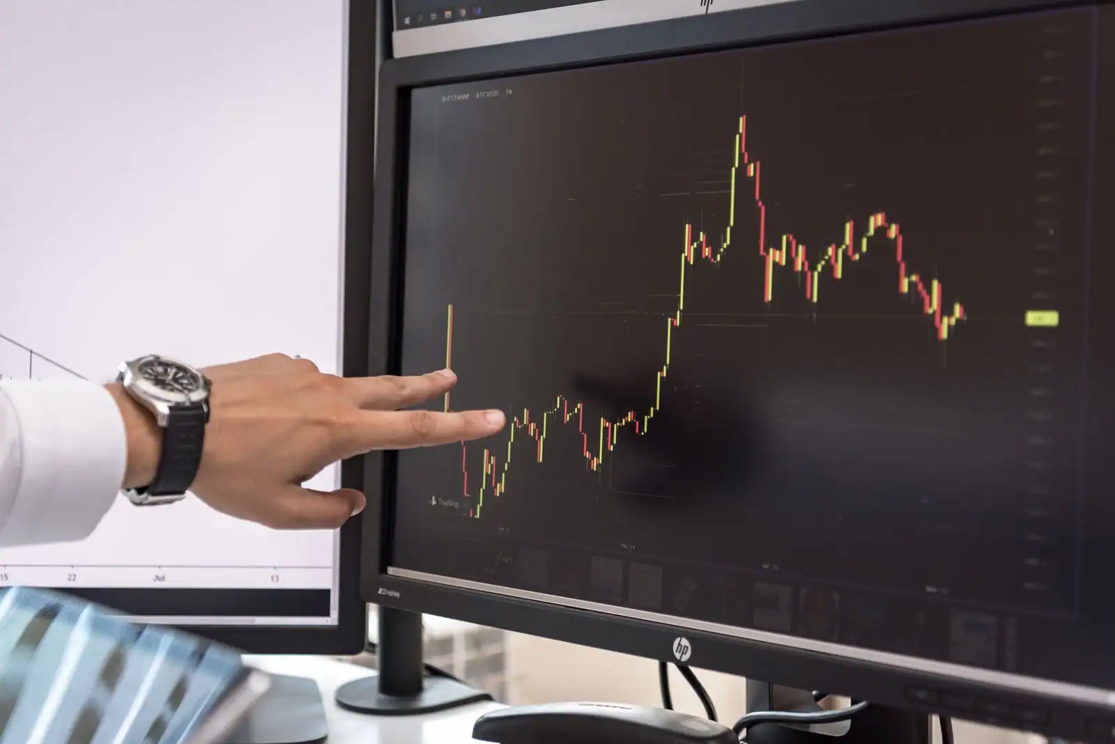 Hand pointing at a volatile crypto price chart on a monitor